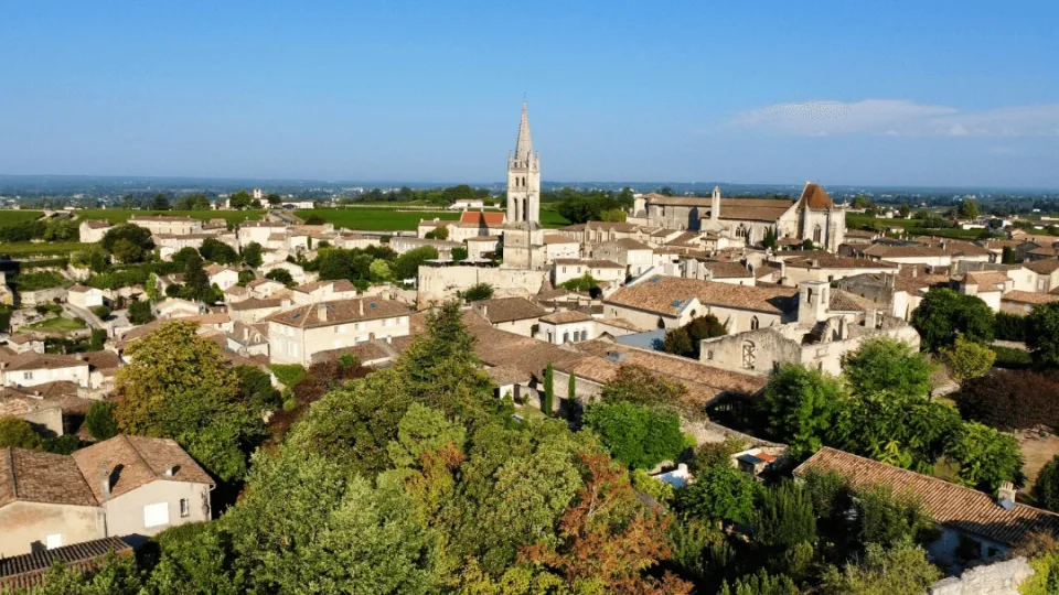 Vue aérienne de la cité médiévale de Saint-Émilion avec son clocher emblématique, ses toits en pierre blonde et les vignobles en arrière-plan.