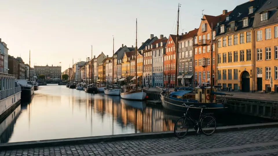 Le canal de Nyhavn à Copenhague à l'heure dorée, maisons colorées alignées le long de l'eau, voiliers en bois amarrés et un vélo posé contre le quai pavé